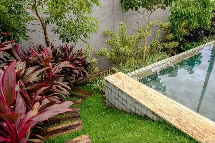 Piscina com revestimento azul, vegetação natural e pisante para jardim de madeira. Projeto de Andréa Esteves